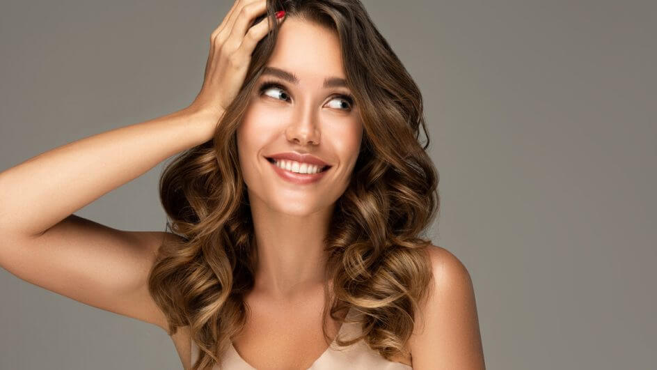 Mulher com a mão no cabelo sorrindo e olhando para o lado