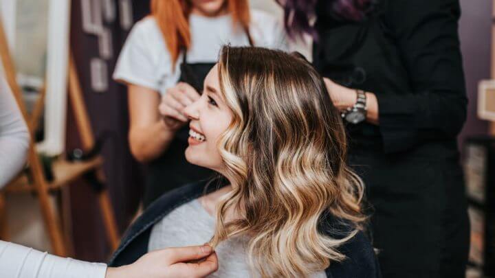 Mulher loira de lado e pessoa segurando o cabelo dela
