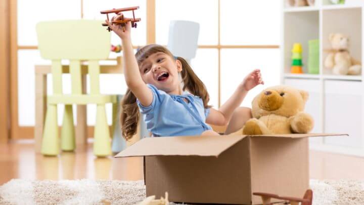 Garota brincando de piloto fingindo estar voando uma caixa de papelão no quarto