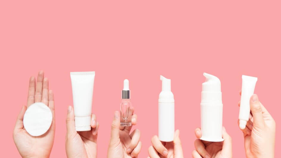 Mãos femininas segurando embalagens de produtos em frente a um fundo rosa