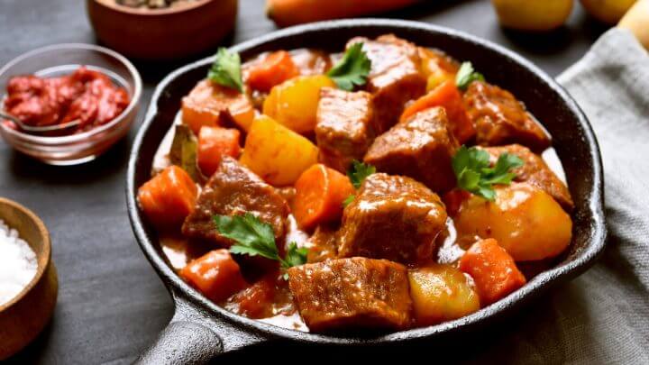 Panela preta com ensopado de carne com batata e cenoura polvilhado com coentro