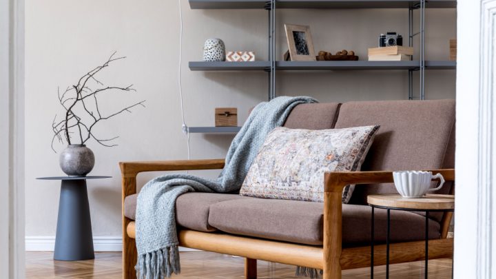 Sala de estar no apartamento aconchegante com sofá de madeira marrom, mesa de centro, estante cinza, travesseiro, xadrez e acessórios elegantes