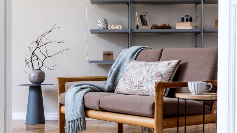 Sala de estar no apartamento aconchegante com sofá de madeira marrom, mesa de centro, estante cinza, travesseiro, xadrez e acessórios elegantes
