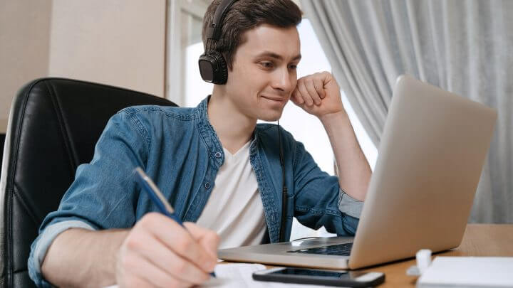 Menino sorrindo usando fone de ouvido estudando em um notebook