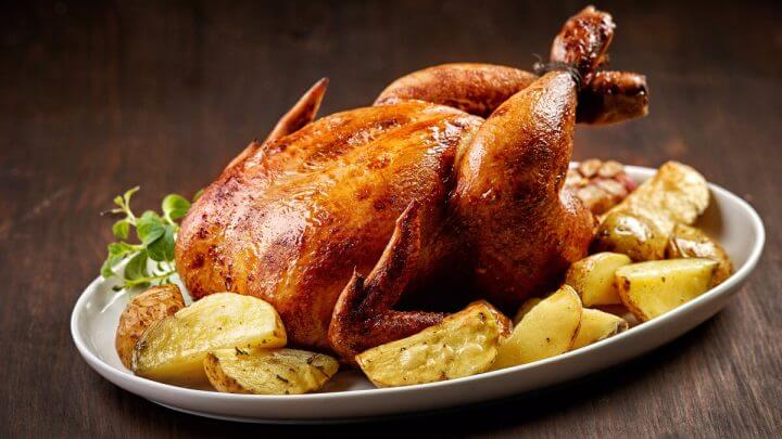 Frango assado em uma travessa branca com batatas