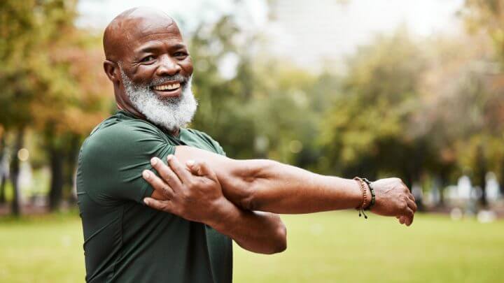Homem com camiseta verde e barba branca alongando o braço