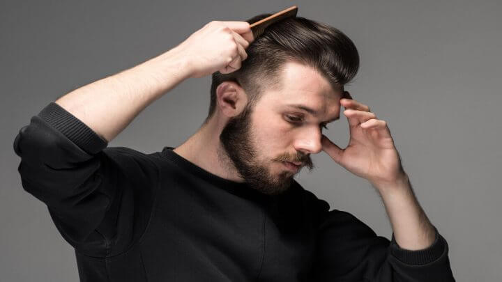 Homem, com camiseta preta e barba, penteando o cabelo.