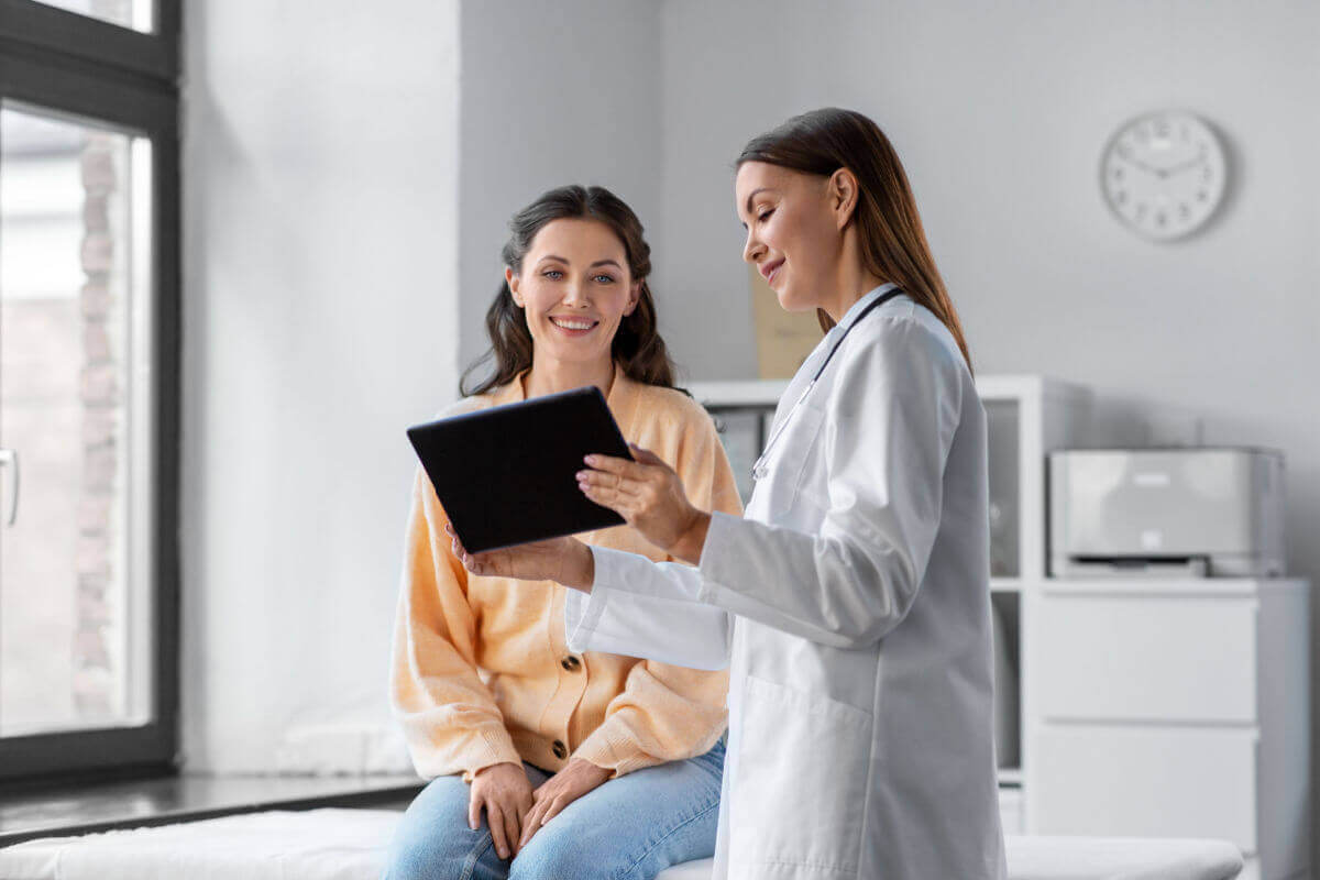 Médica com prancheta na mão atendendo a uma outra pessoa do sexo feminino