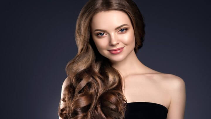 Mulher com cabelo longo cacheado sorrindo em frente a um fundo azul