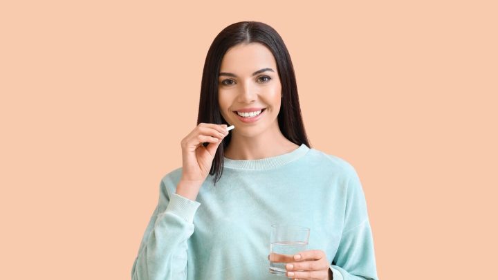 Mulher vestindo blusa azul sorrindo e tomando remédio