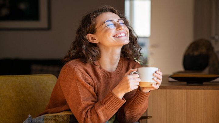 Mulher sentada segurando caneca e sorrindo