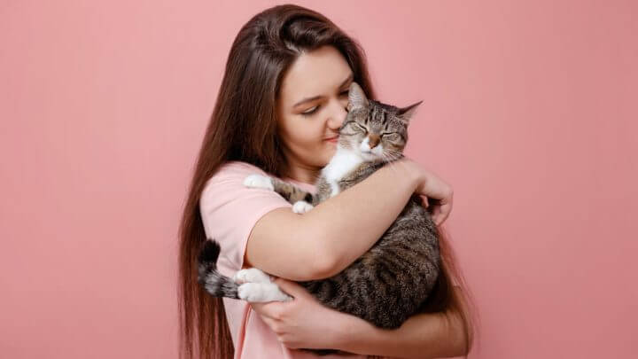 Mulher segurando gato no colo em fundo rosa