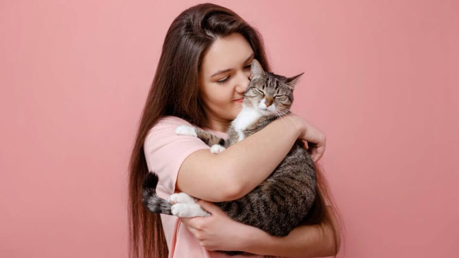 Mulher segurando gato no colo em fundo rosa