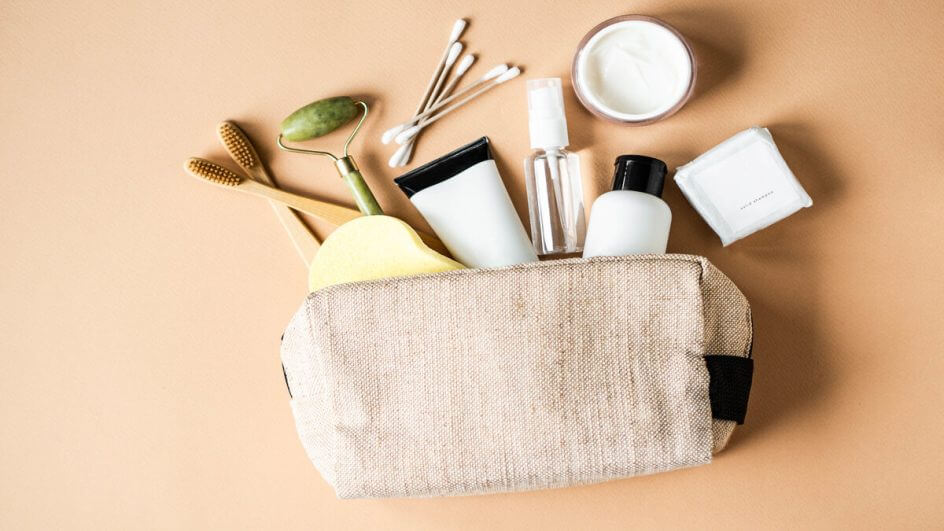 Nécessaire em cima de um fundo bege com produtos saindo de dentro dela