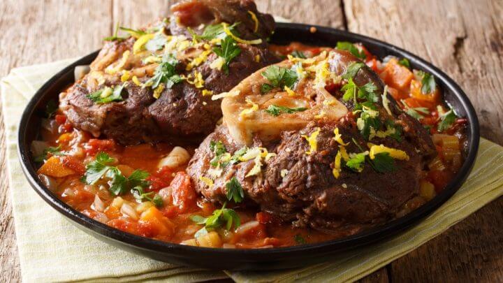 Prato preto com dois pedaços de ossobuco com molho de tomate e temperos
