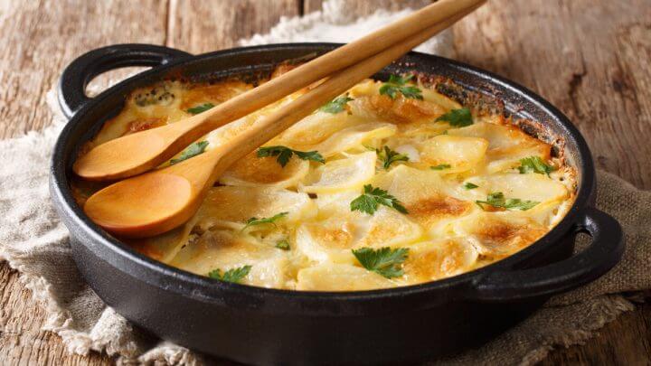 Panela preta com batata e queijo gratinado em cima de uma mesa de madeira