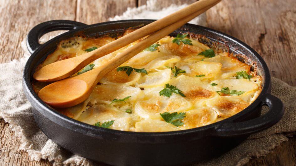 Panela preta com batata e queijo gratinado em cima de uma mesa de madeira