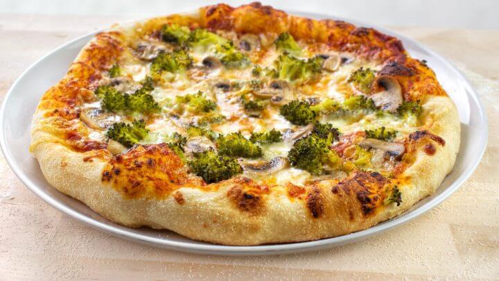 Pizza de brócolis com queijo e cogumelos em cima de uma mesa de madeira