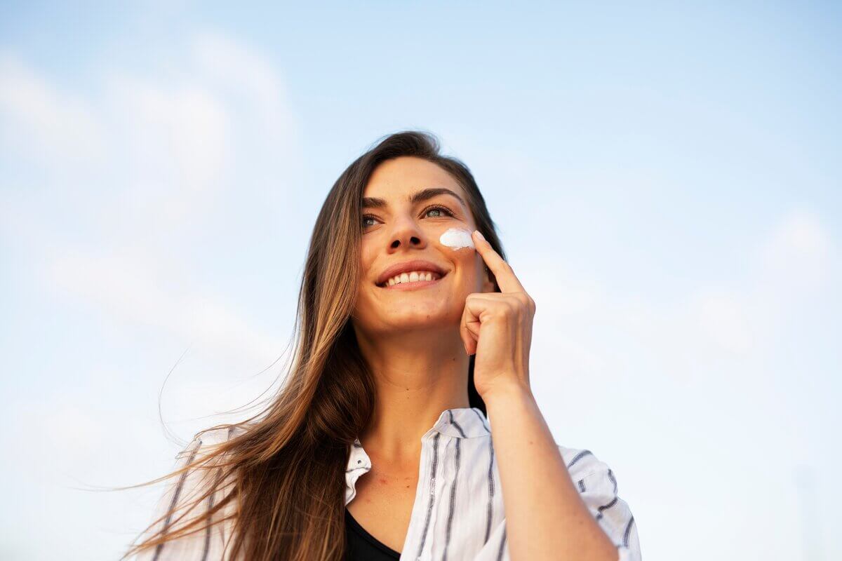 Mulher sorrindo passando protetor solar no rosto