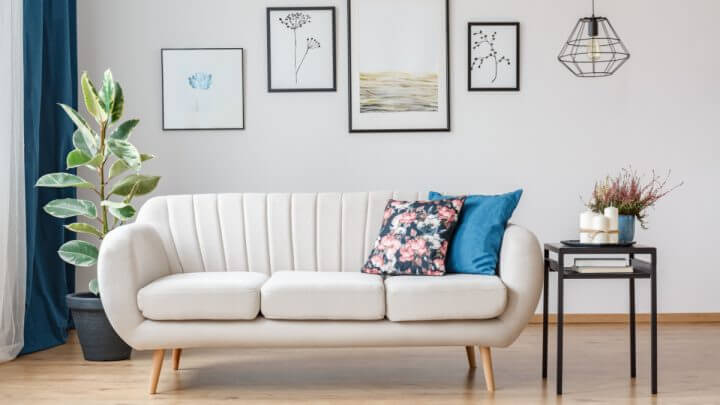 Interior de uma sala de estar com sofá bege, quadros com molduras pretas na parede, mesa preta e almofadas coloridas