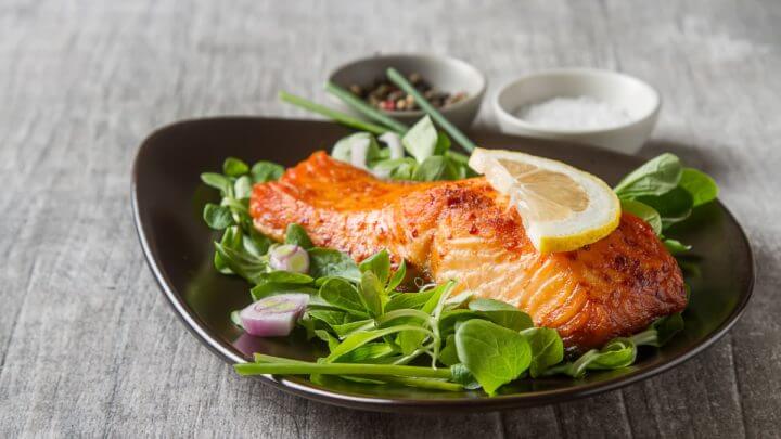 Filé de salmão em um prato preto com salada decorado com uma fatia de limão