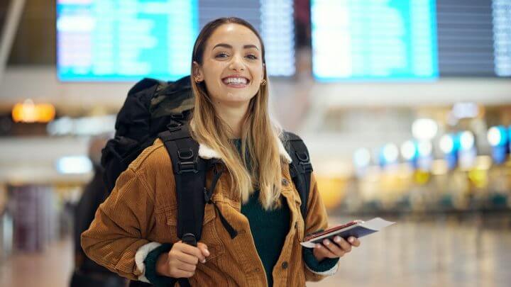 Mulher sorrindo segurando passaporte dentro de um aeroporto