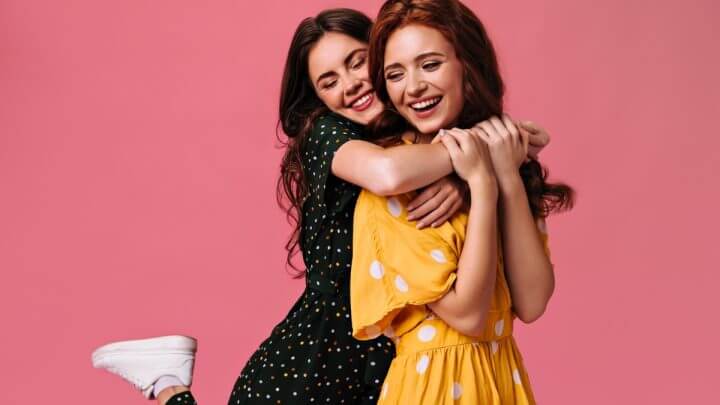 Duas mulheres se abraçando em frente a um fundo rosa