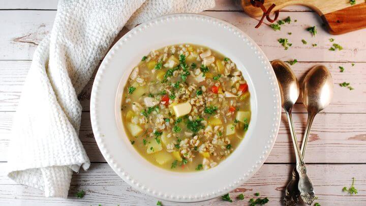 Sopa de cevadinha com frango em prato branco e colher ao lado