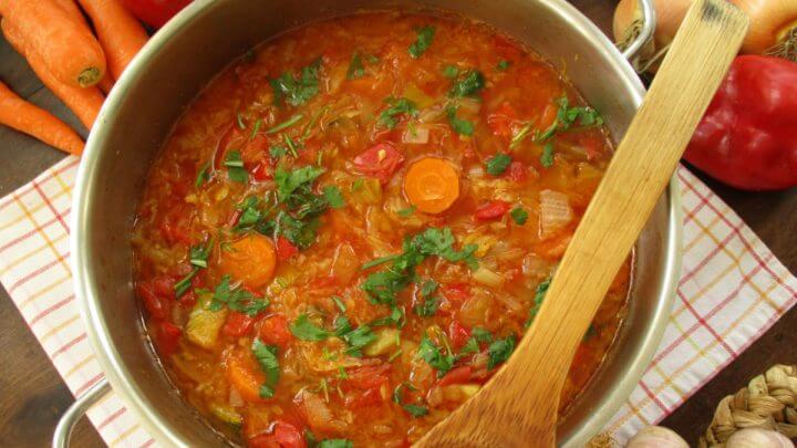 Sopa de repolho colorida em panela de ferro com colher de pau e vegetais em volta