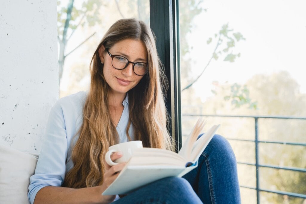 Mulher lendo livro e com uma xÃcara na mão em um lugar calmo